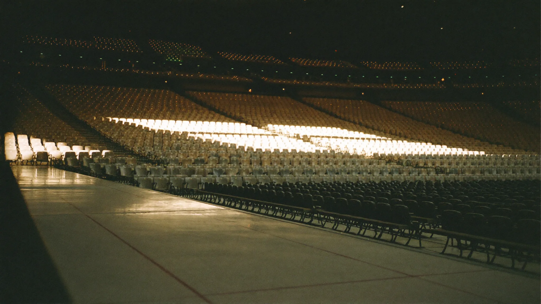 An empty major-market arena bowl before doors open, a single shaft of warm light crossing the seats.